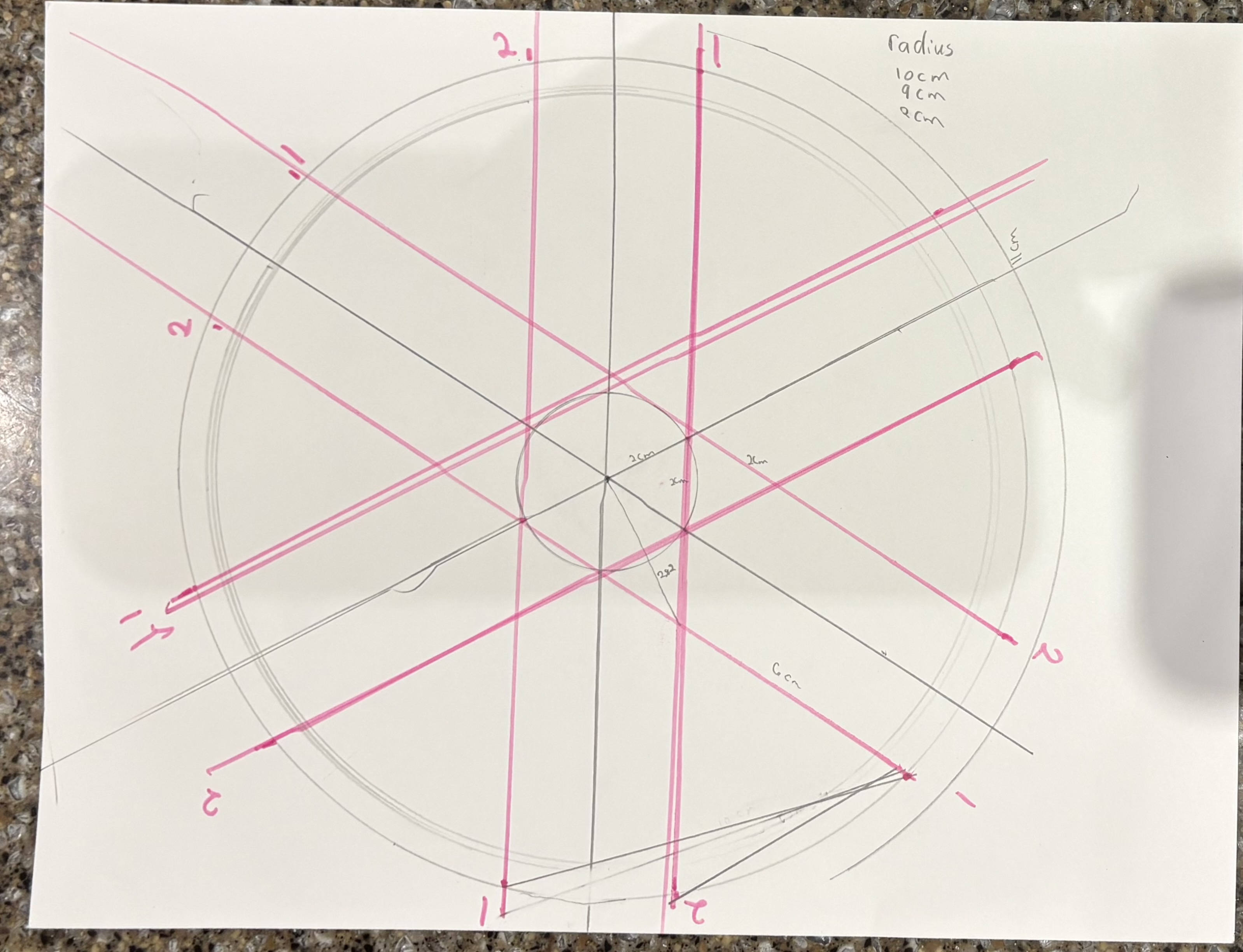 Hand-drawn geometry sketch in pencil and pink marker, showing circles, spokes, and radius annotations
